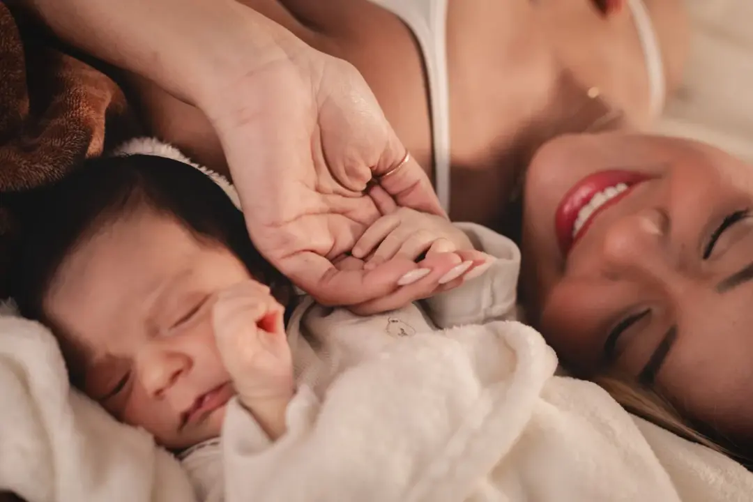 A mother and her newborn holding hands, capturing a tender moment of love.